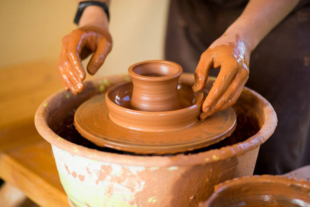 Ręce garncarza robią naczynia garncarskie na kole garncarskim. Rzeźbiarz w warsztacie sprawia, że glina produkt - Zdjęcie, obraz