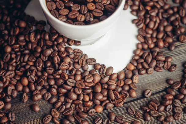 coffee beans on a wooden background and a cup on a saucer close-up macro photography - 写真・画像