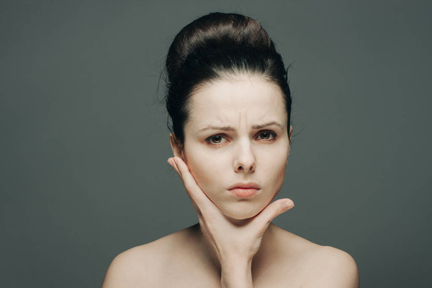 woman with bare shoulders gathered hair discontent hand on face - Photo, Image
