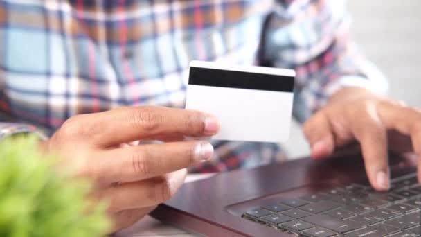 мужчина держит в руках кредитную карту и совершает покупки онлайн с помощью ноутбука  - Кадры, видео