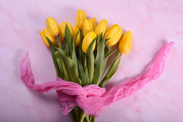 μπουκέτο από κίτρινες τουλίπες με ροζ ύφασμα σε ροζ φόντο. Ημέρα του Αγίου Βαλεντίνου, Ημέρα της Γυναίκας και έννοια Ημέρα της Μητέρας. - Φωτογραφία, εικόνα