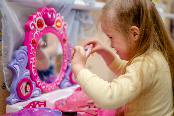 Desarrollo y educación de un niño pequeño con síndrome de Down. Niña con síndrome de Down juega princesa en la habitación de los niños. - Foto, Imagen