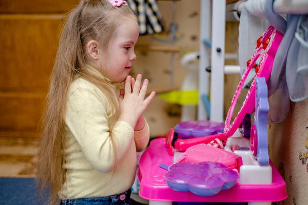 Egy Down-szindrómás kisgyermek fejlődése és oktatása. Kislány Down-szindrómával játszik hercegnő a gyerekszobában. - Fotó, kép