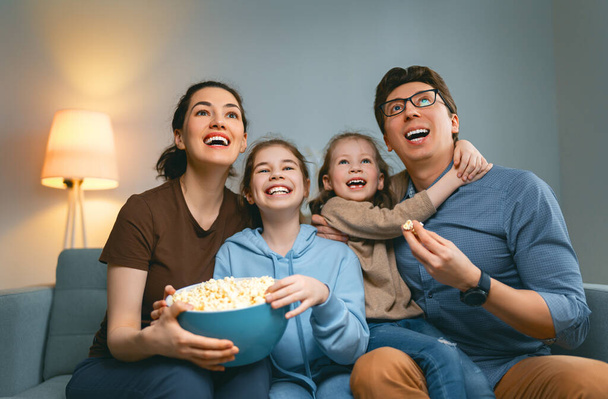 Happy family watching TV with popcorn  at home. Mother, father and daughters spending time together. - Valokuva, kuva