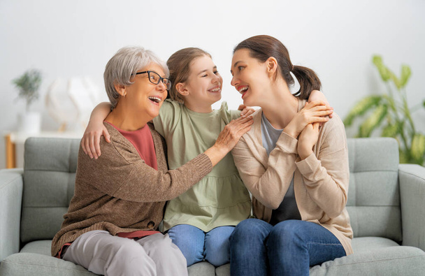 A nice girl, her mother and grandmother are hugging and  enjoying spending time together at home.  - Foto, Imagem