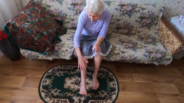 Senior mulher aplicando creme em suas pernas sentado no sofá - Filmagem, Vídeo