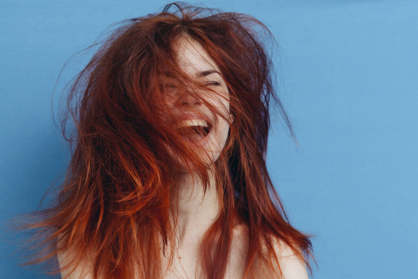 happy woman with red hair on blue background fun emotions tousled curls - Photo, Image