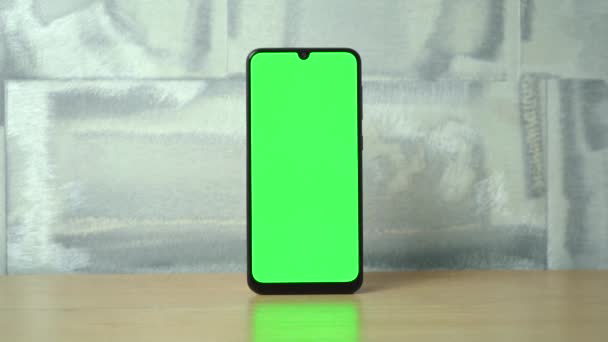 telefoon met een groen scherm staat op een houten tafel. - Video