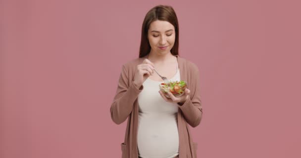 Clean eating. Studio shot of happy pregnant woman enjoying fresh vegetable salad over pink background - Footage, Video