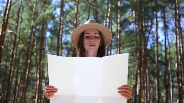 Μια γυναίκα με καπέλο κοιτάζει ένα χάρτη στο δάσος. Concept πεζοπορία, τουρισμός. - Πλάνα, βίντεο
