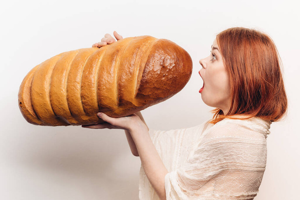 zijaanzicht van mooie roodharige vrouw met vers brood in handen - Foto, afbeelding