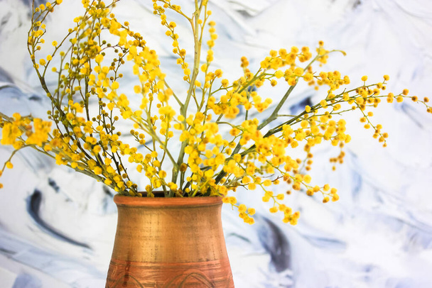 茶色い土の花瓶に黄色のミモザの花の花束。黒と白のブラシストロークの背景に黄色の春の花。ゴールデンアカシアのディールバータが咲きます。母の日の贈り物3月8日イースター. - 写真・画像