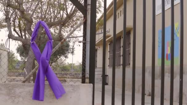 Symbool van een paars lint gemaakt van stof en vastgebonden met flenzen aan een metalen poort van een gesloten en ongefocust educatief centrum. Symbool ter herdenking van Internationale Vrouwendag, 8 maart - Video