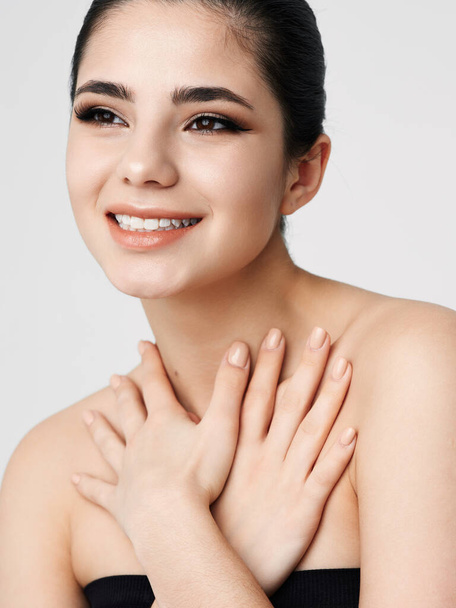 glimlachende vrouw gezicht met make-up naakt schouders handen in de buurt van de nek - Foto, afbeelding