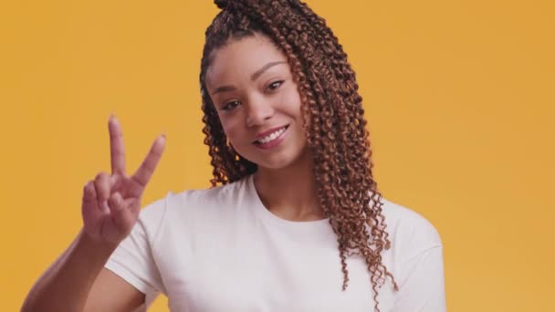 Frieden für alle. Fröhliche afrikanisch-amerikanische Frau zeigt V-Zeichen und lächelt, bewegt ihren Körper, orangefarbener Studiohintergrund - Filmmaterial, Video