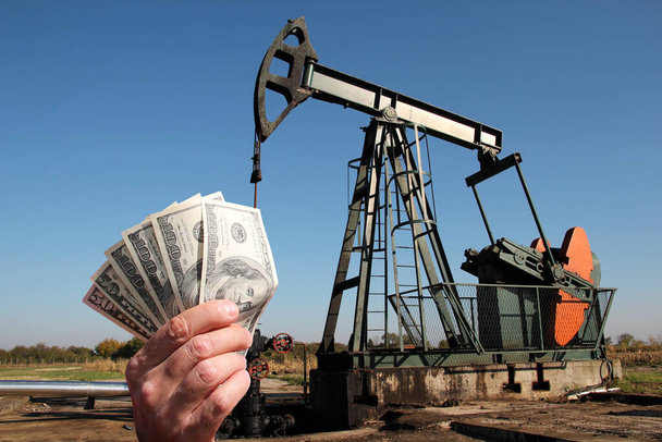 Αντλία αργού πετρελαίου πίσω από το χέρι με χαρτονομίσματα του δολαρίου ΗΠΑ - Φωτογραφία, εικόνα