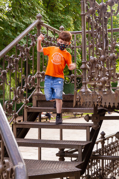 Söpö punapää poika kasvoissa naamio ja oranssi t-paita kävelemässä portaita metalli bändi seistä aurinkoisena päivänä - Valokuva, kuva