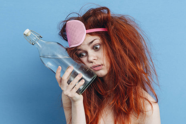 mulher ruiva emocional com máscara de sono garrafa de álcool ressaca nas mãos - Foto, Imagem