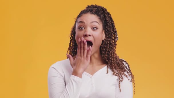 . Studioporträt einer überraschten afrikanisch-amerikanischen Frau, die erstaunt ihren offenen Mund bedeckt, orangefarbener Hintergrund - Filmmaterial, Video