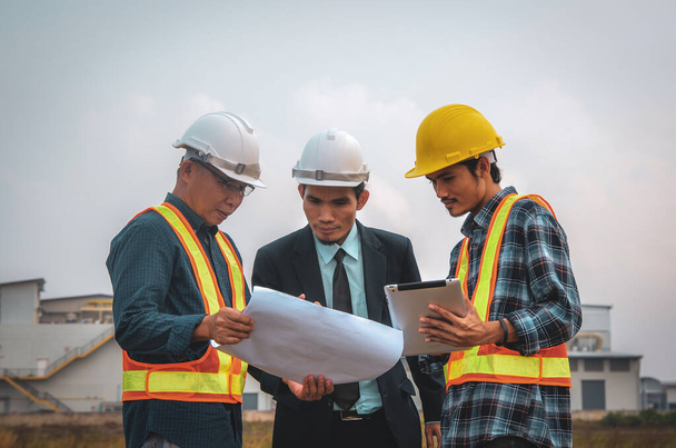 Construction engineers speak at the construction site, with a tablet and blueprint in the hand. - Photo, Image