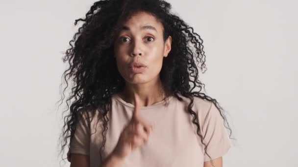 Jonge aantrekkelijke Afro-Amerikaanse vrouw houdt de vinger over de lippen waaruit blijkt dat het geheime uitdrukking over witte achtergrond. Zeg het niet. - Video