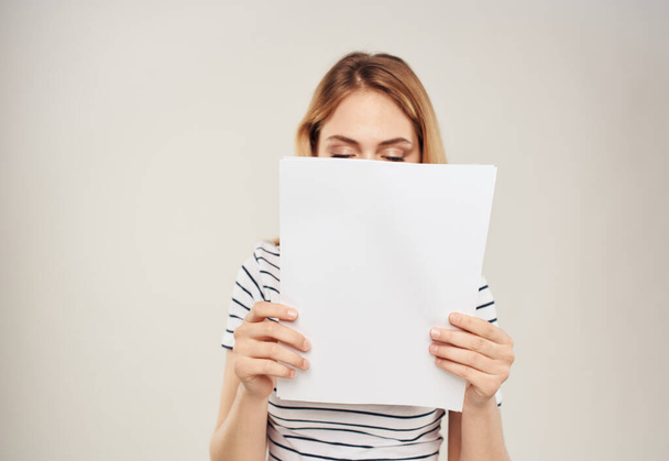 Женщина в полосатой футболке светлые волосы и белый лист бумаги на бежевом фоне - Фото, изображение