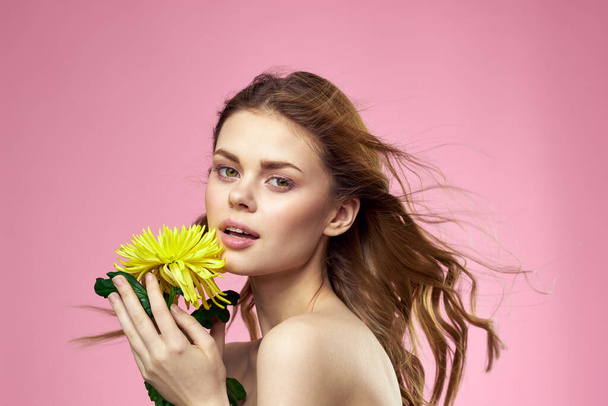 Όμορφο κορίτσι με ένα κίτρινο λουλούδι σε ροζ φόντο γυμνό ώμο μακιγιάζ - Φωτογραφία, εικόνα