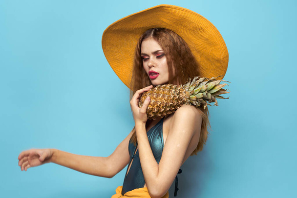 nő strand kalap ananász gazdaság fürdőruha egzotikus gyümölcsök kék háttér nyaralás - Fotó, kép