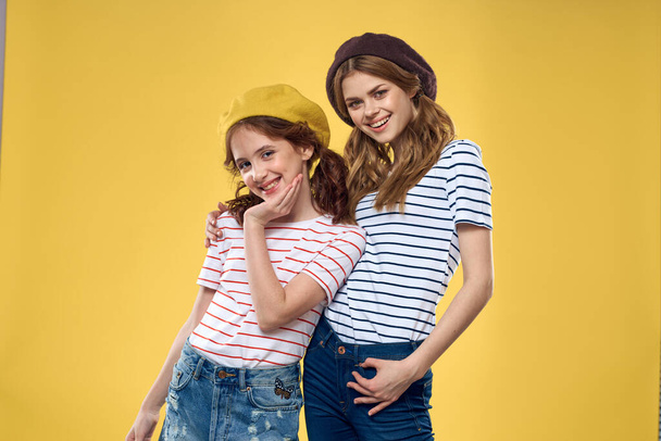 смешные мама и дочь в шляпах мода веселье радость семьи желтый фон - Фото, изображение
