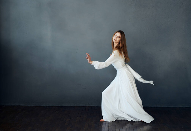 Очаровательная леди в белом платье на сером фоне танцует жестикулируя руками модели - Фото, изображение
