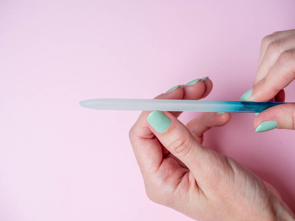 una mujer misma está archivando sus uñas con una lima de uñas en su mano sobre un fondo rosa. Cuidado de uñas en casa. Belleza y Salud - Foto, imagen