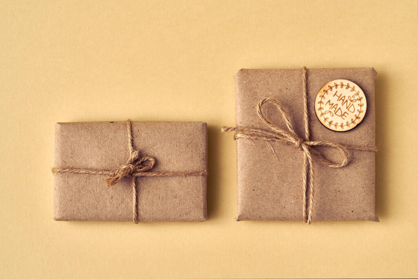 Two presents wrapped in ecological recycled paper with wooden inscription Handmade on a yellow background - Photo, Image