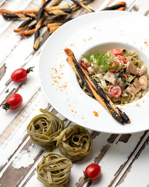 Tradiční italská jídla těstoviny a rajčata na bílém podnose. Talíř s jídlem na pozadí dřevěného kuchyňského stolu. Gurmánská italská kuchyně. Horní pohled - Fotografie, Obrázek