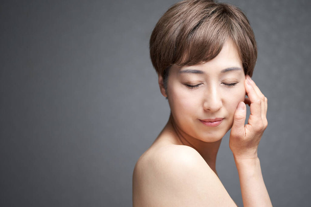 Uma mulher japonesa de meia-idade que coloca a mão na bochecha e fecha os olhos - Foto, Imagem