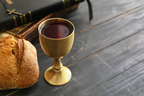Chalice of wine with bread and Holy Bible on dark wooden background - Photo, Image
