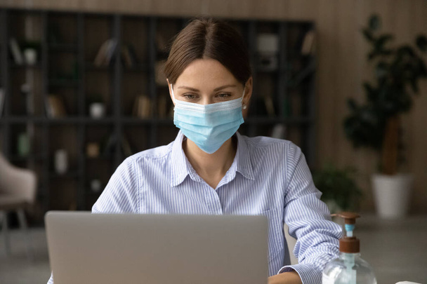 Caucasian female employee in facemask work on laptop - Photo, image