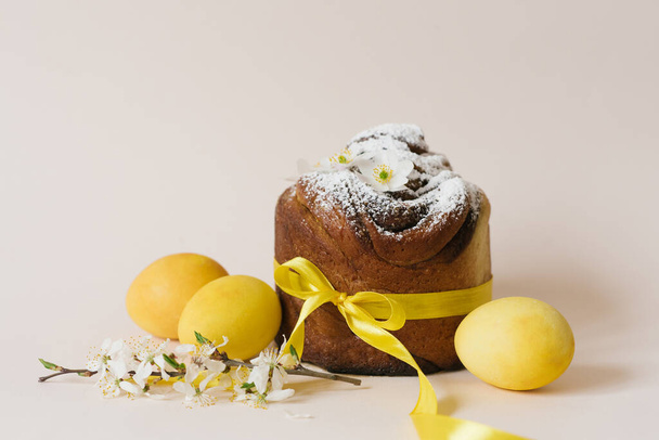 Pasen samenstelling van zoete broodkoek, witte bloemen en gele eieren op een lichte achtergrond. Orthodox paasbrood. Een feestelijk ontbijtconcept met ruimte voor tekst. - Foto, afbeelding