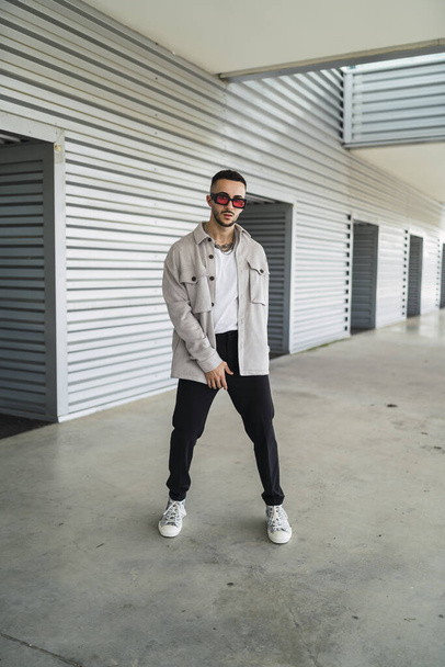 A young fashionable man wearing casual clothes and sunglasses posing outdoors - Foto, immagini