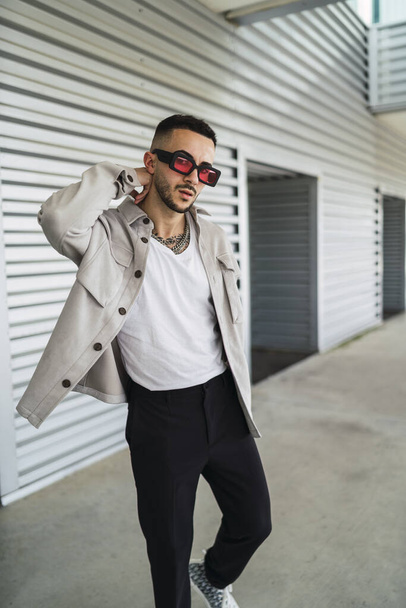 A young fashionable man wearing casual clothes and sunglasses posing outdoors - Foto, Bild