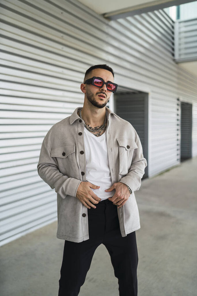 A young fashionable man wearing casual clothes and sunglasses posing outdoors - Fotografie, Obrázek