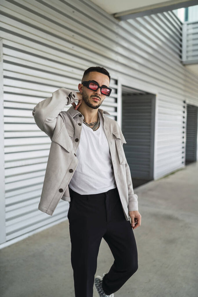 A young fashionable man wearing casual clothes and sunglasses posing outdoors - Valokuva, kuva