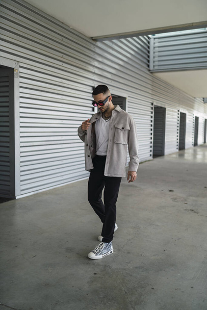 A young fashionable man wearing casual clothes and sunglasses posing outdoors - Photo, image