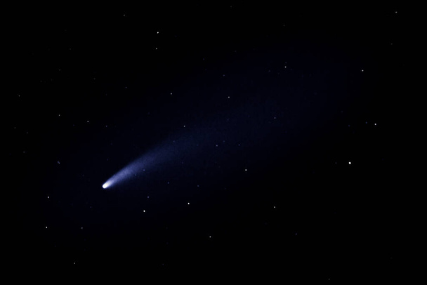 El cometa Neowise vuela más allá de la tierra, visto desde abajo en el cielo oscuro. El cometa deja una cola característica detrás de él. Una cola de cometa es una corriente de gases y polvo que emana de un cometa. - Foto, imagen