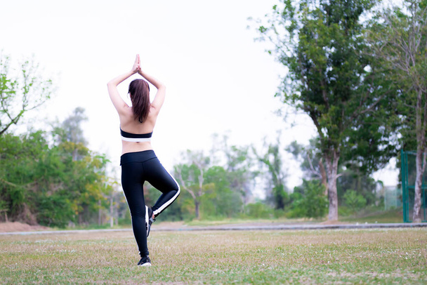 Rückansicht einer Frau, die Yoga in der Natur macht. Die Menschen posieren mit den Händen über dem Kopf und stehen auf einem Bein. Yoga-Baumpose. Leichte Übung. - Foto, Bild