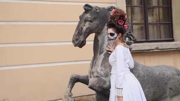 Chica en la imagen de un demonio con maquillaje para Halloween, junto a la estatua del caballo, Chica con maquillaje de Halloween, Santa Muerte - Imágenes, Vídeo