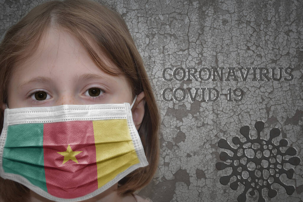 Little girl in medical mask with flag of cameroon stands near the old vintage wall with text coronavirus, covid, and virus picture. Stop virus - Photo, Image
