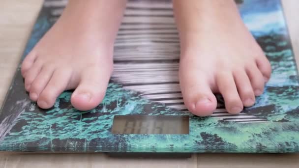 Adolescente bambino su bilance misurare il peso. Il bambino controlla il suo peso a piedi nudi. 4K - Filmati, video