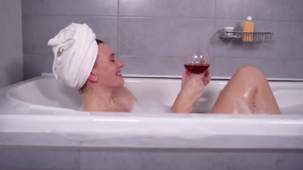 Szczęśliwa kobieta kąpie się w wannie z białą pianką na twarzy radosne emocje. Trzyma kieliszek wina i uśmiecha się. Pani odpoczywa w domu.. - Materiał filmowy, wideo