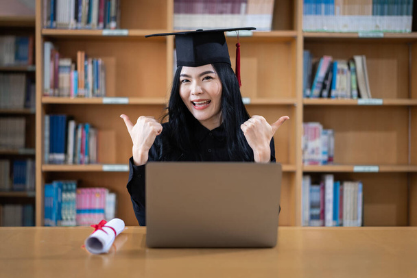 Una joven graduada universitaria asiática expresando alegría y emoción por celebrar su logro de graduarse frente a una computadora portátil haciendo una videollamada remota a sus padres en casa - Foto, imagen