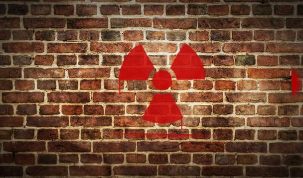 Radiation and nuclear energy warning symbol spray painted on the brick wall. Graffiti art concept of radioactive hazard and danger. Urban abstract artwork. Airbrush paint with sign template in hand. - Photo, Image